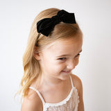 Young girl wearing a black velvet bow headband on a white background