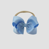 Light blue hair bow on a nude nylon headband against a white background