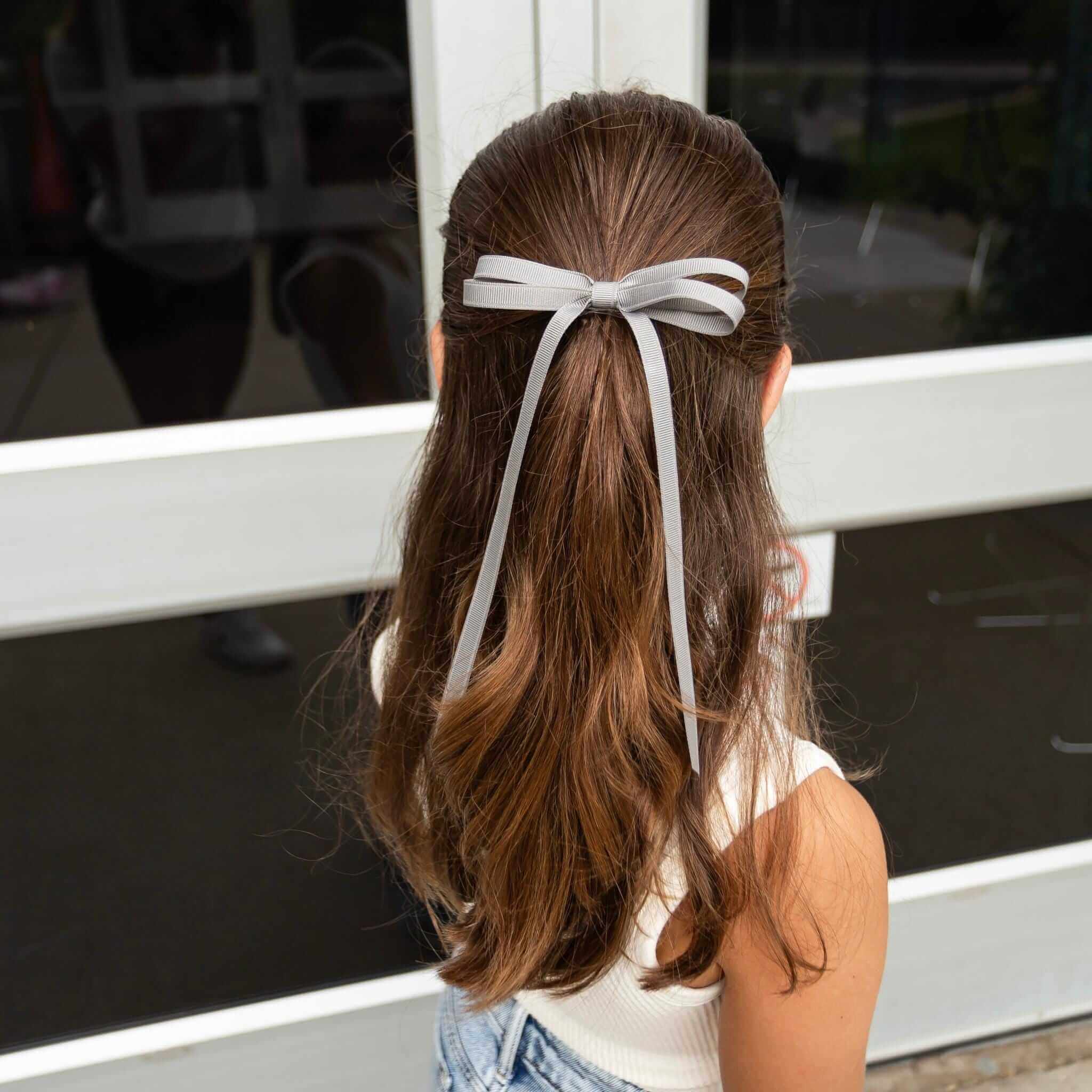 Olivia Grosgrain Hair Bow in gray, tied in a ponytail on a girl's hair, showcasing a cute and polished look.