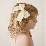 Young girl with blonde hair wearing the Kayla velvet bow in ivory against a plain background