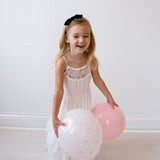 Young girl in a white dress holding balloons against a plain background