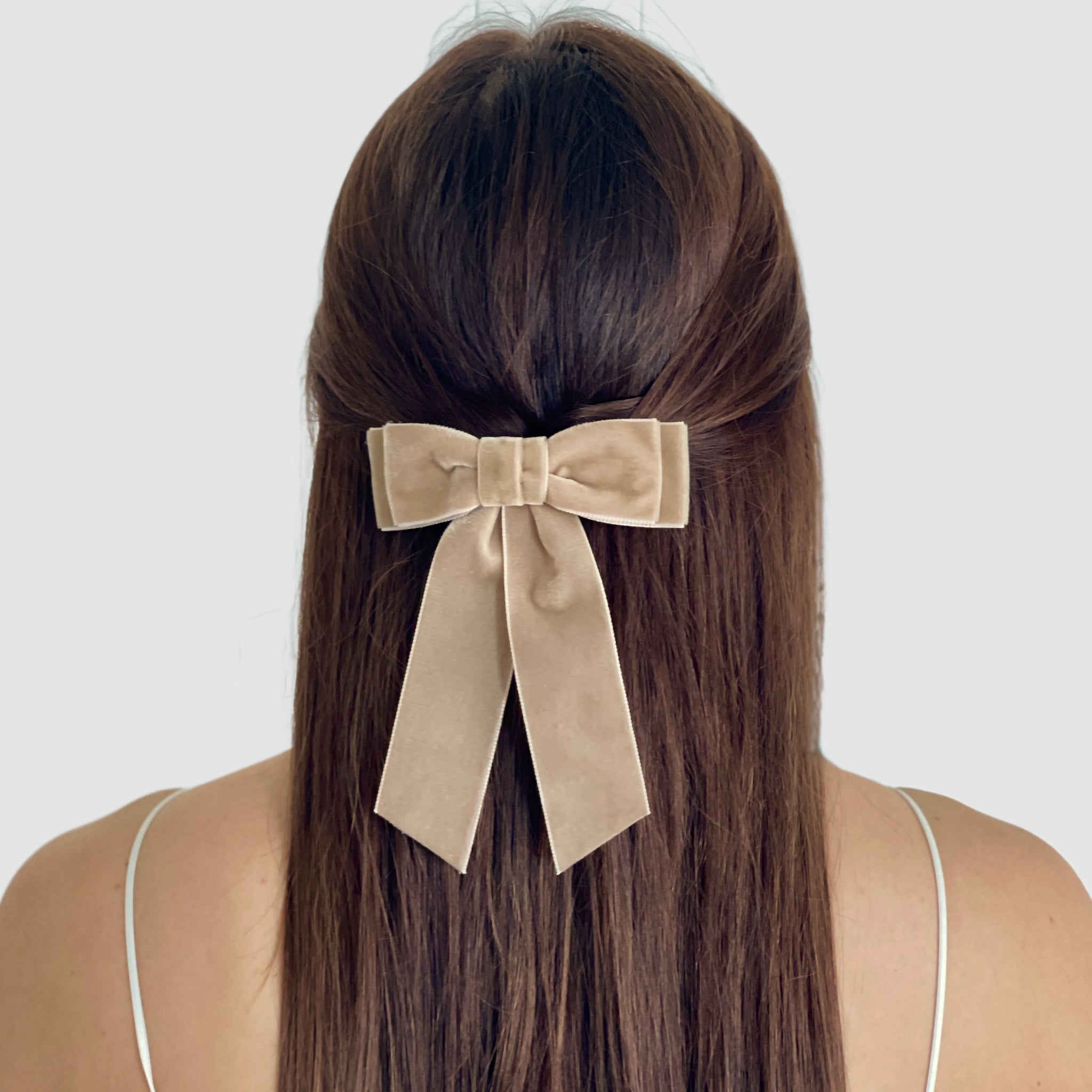 Model with long brown hair wear Mia velvet hair bow in taupe in a half-up hairstyle.