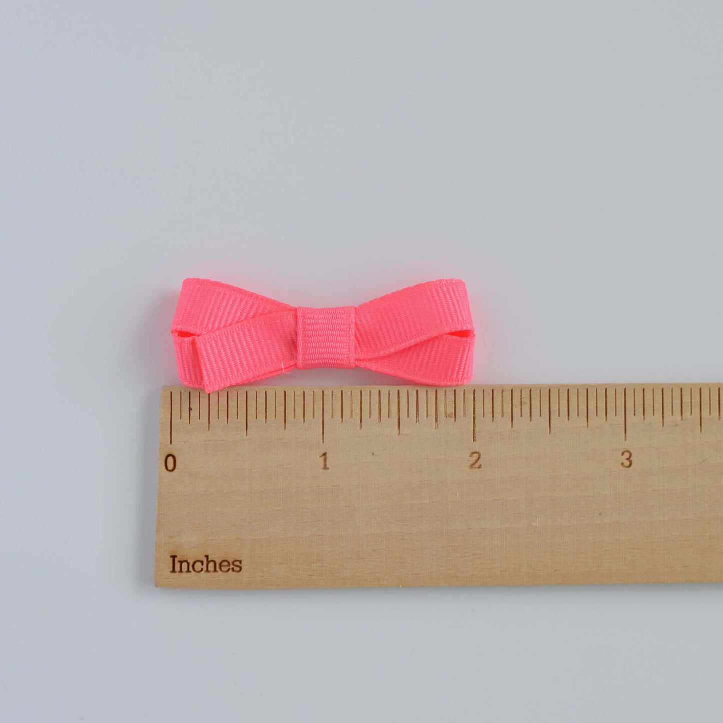 Bright pink mini grosgrain hair bow next to ruler for size reference, perfect for baby and toddler girls, with a snap clip and no-slip grip.
