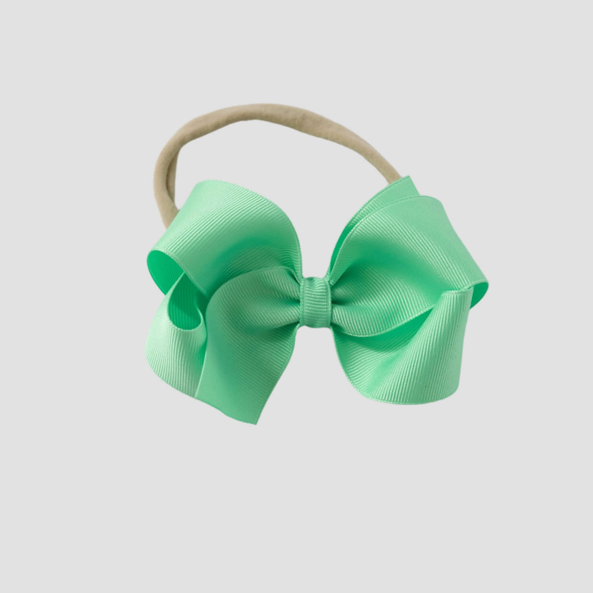 Mint green hair bow on a nude nylon headband on a white background