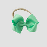 Mint green hair bow on a nude nylon headband on a white background
