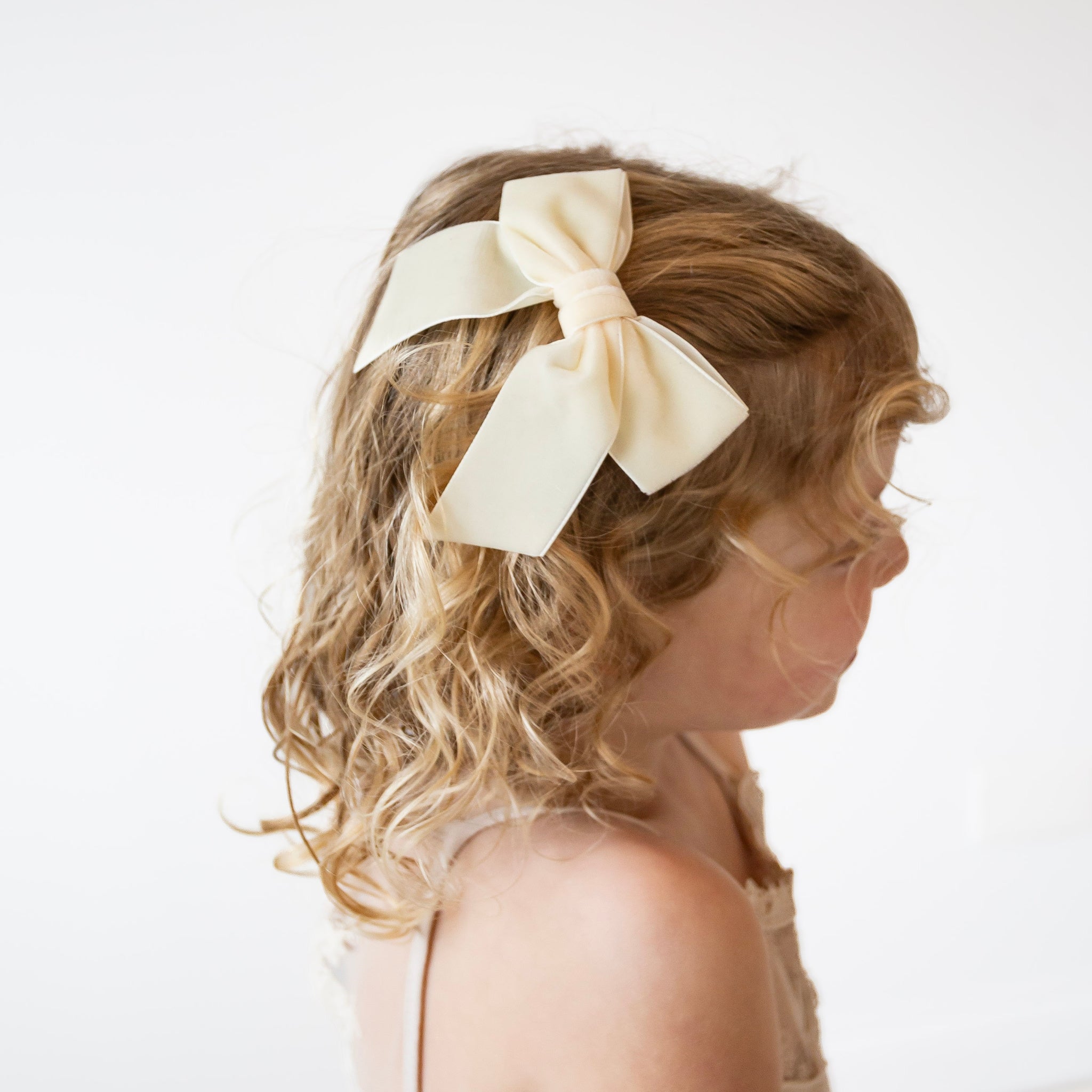 Girl wearing Flora velvet bow in ivory on a white background.