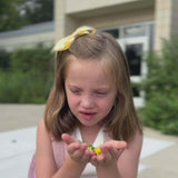 Young girl wearing yellow sailor bow while blowing flowers into the air.