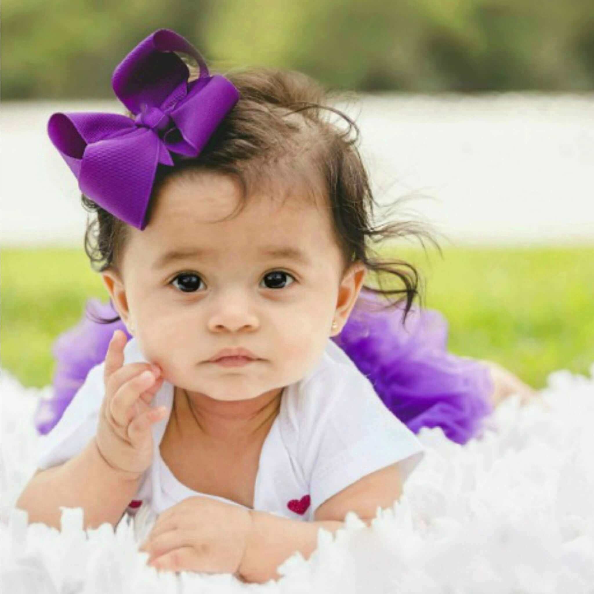 Baby with a purple bow and tutu sitting on grass