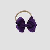 Purple hair bow on a nude nylon headband against a white background