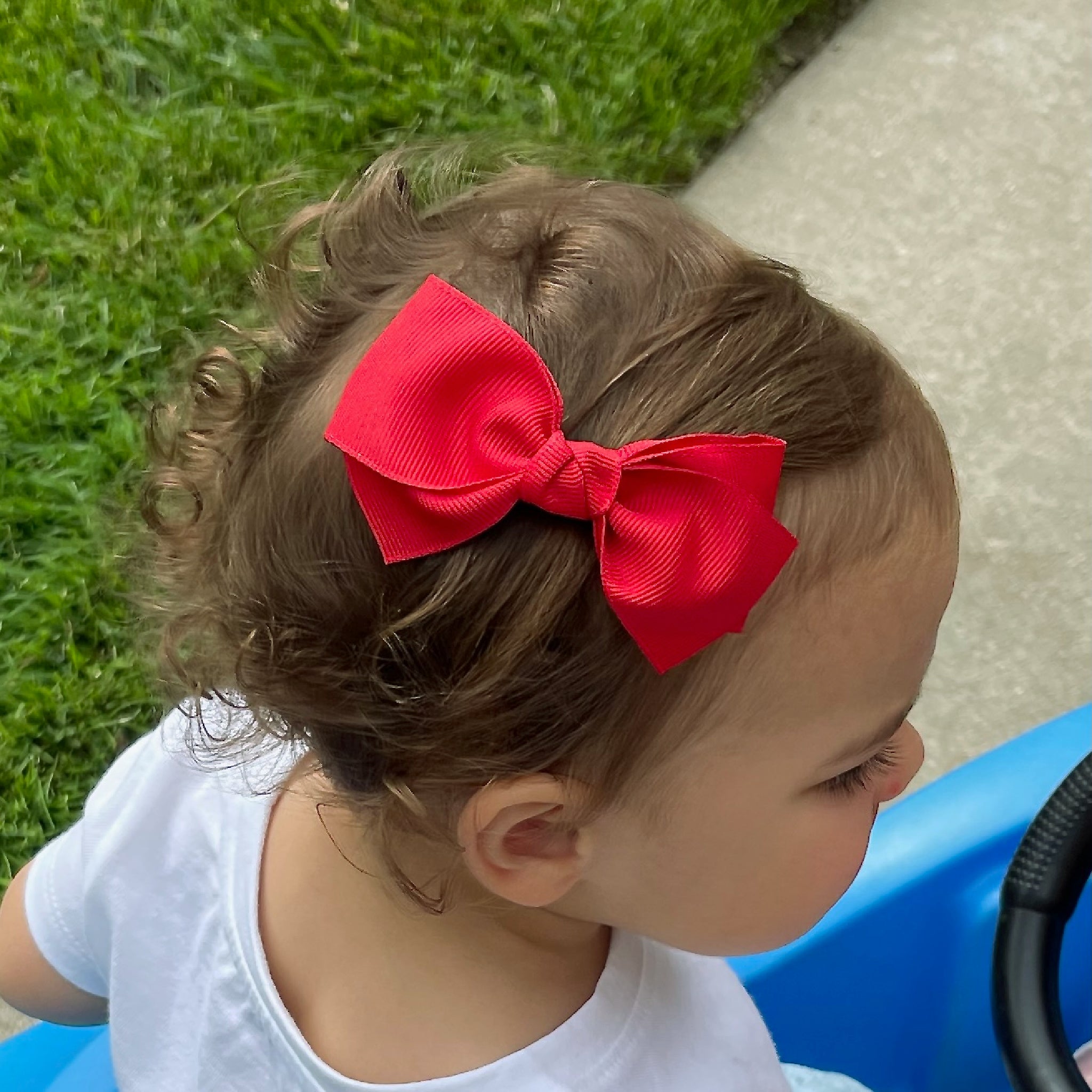 Child with a red bow in their hair outdoors