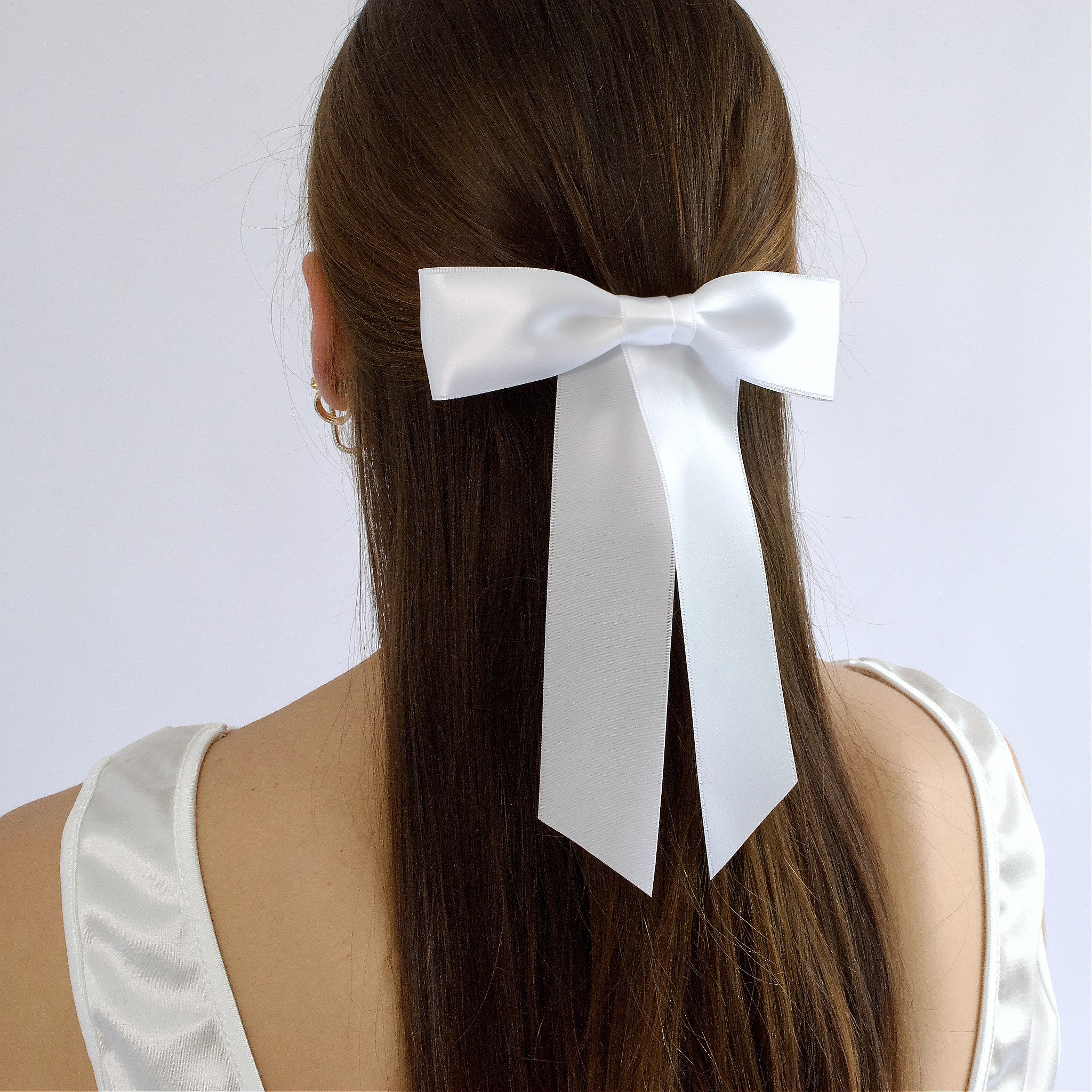 White satin Zoe petite hair bow on a model,wearing  a half up style against a white background