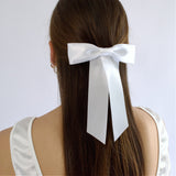 White satin Zoe petite hair bow on a model,wearing  a half up style against a white background