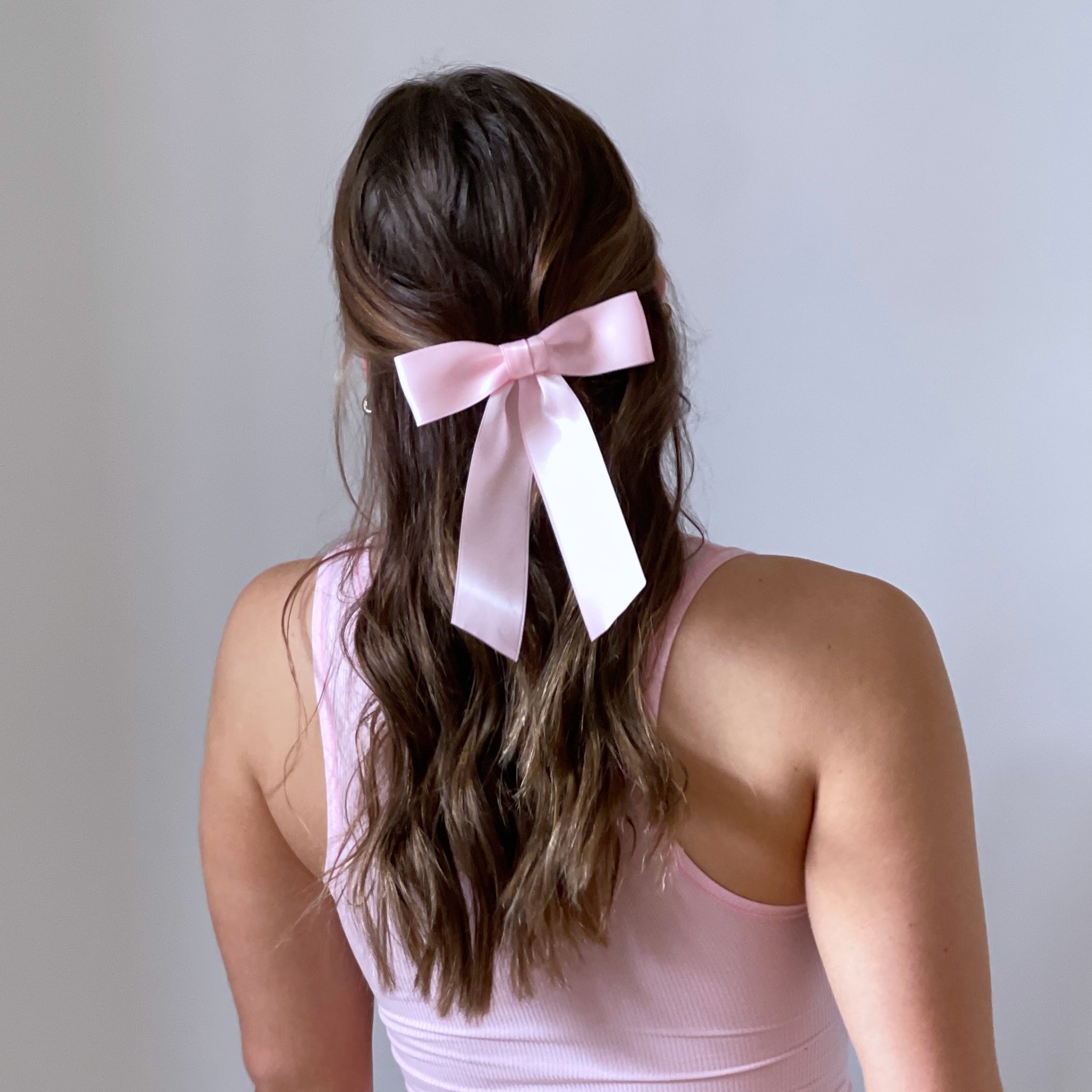 Model is wearing the Zoe Petite Satin Bow in light  pink bow in her hair and wearing a pink sleeveless top against a plain  white background