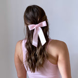 Model is wearing the Zoe Petite Satin Bow in light  pink bow in her hair and wearing a pink sleeveless top against a plain  white background